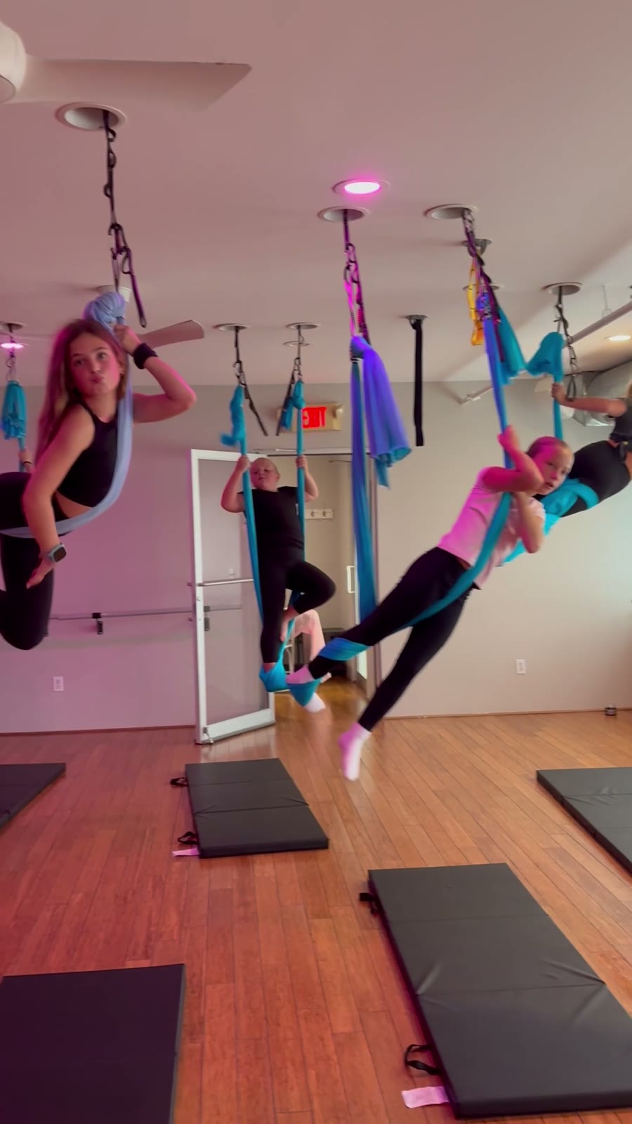 Kids posing in the blue silks during Kids Aerial, smiling, the studio's windows behind them.