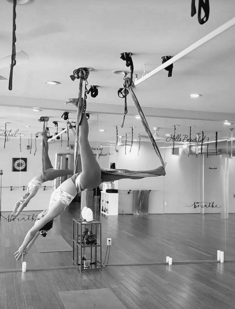A student inverted in the aerial silks, candles on the floor below.