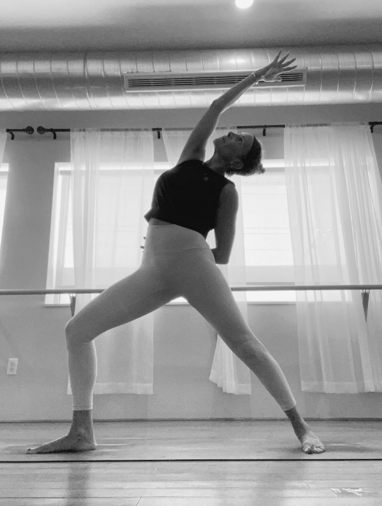 A teacher in reverse warrior by the curtained windows.