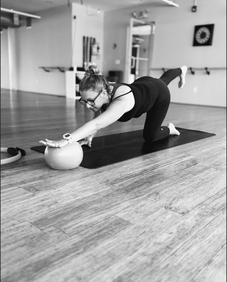 A student in a Pilates bird dog over a ball.
