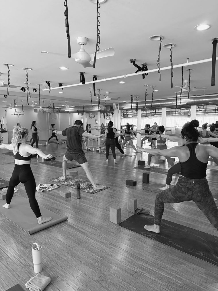 A full class in warrior two across the studio, under the aerial rigging.