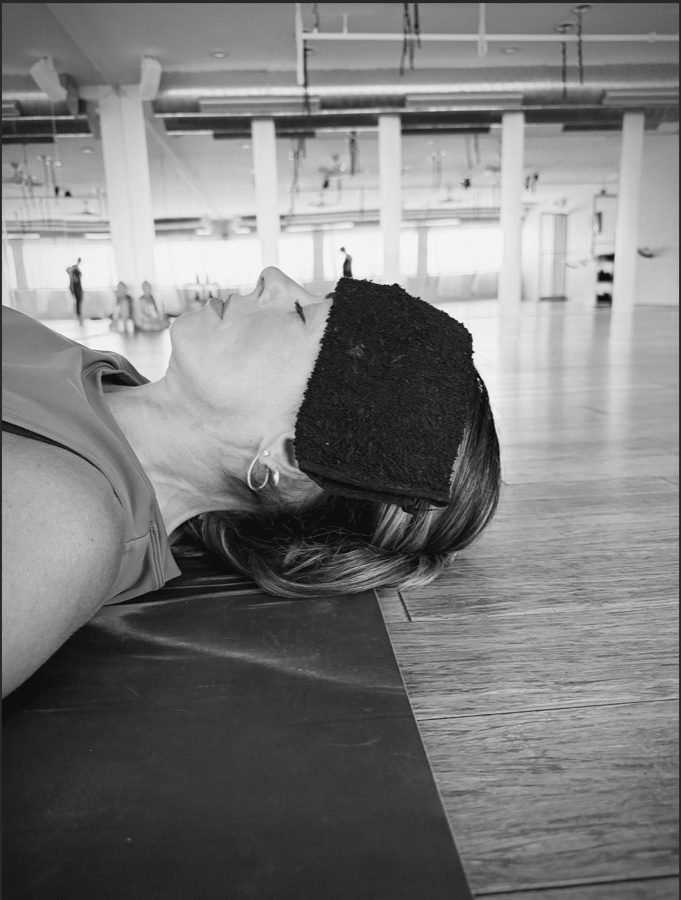 A student resting in savasana with a cool towel.